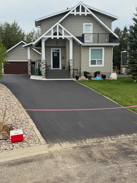 New asphalt driveway leading to a craftsman-style home with stone accents