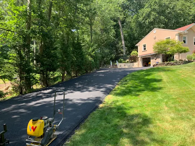 Plate compactor finishing the edges of a newly paved asphalt driveway