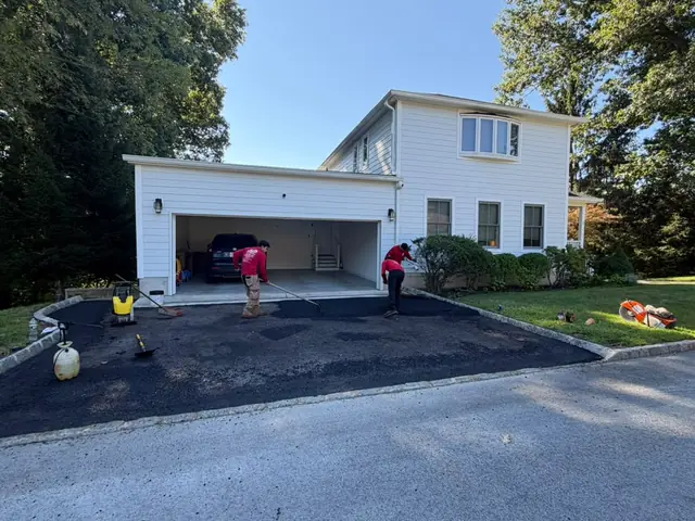 Crew finishing a new asphalt driveway at a two-car garage
