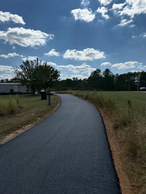 Curved new asphalt driveway through an open grassy field