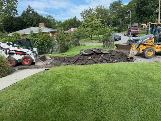 Skid steer and loader removing old driveway material from a residential lot