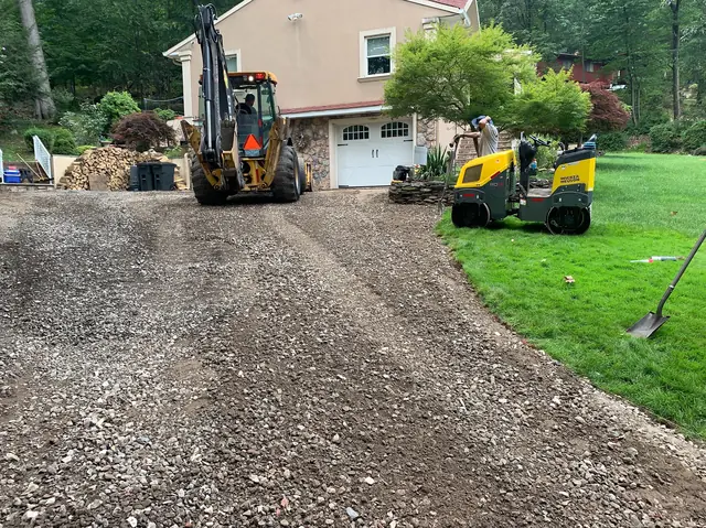 Backhoe and roller preparing the base for a new residential driveway
