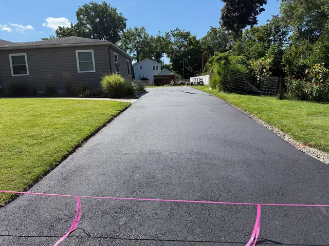 Fresh blacktop driveway with crisp edges next to a well kept lawn
