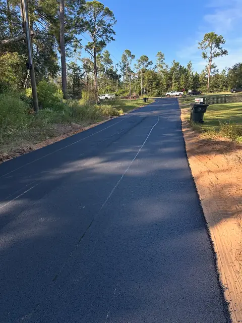 Long freshly rolled blacktop driveway with sandy shoulders
