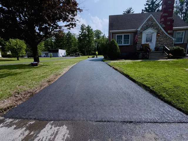 Long residential asphalt driveway leading up to a cape-style home