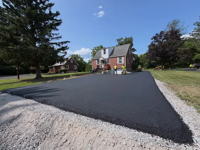 Freshly paved asphalt driveway with compacted stone shoulders in front of a brick house