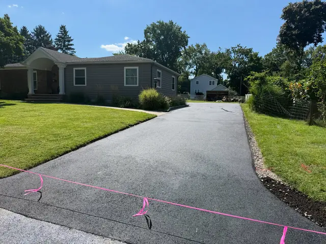 Newly paved asphalt driveway curving toward a ranch-style home