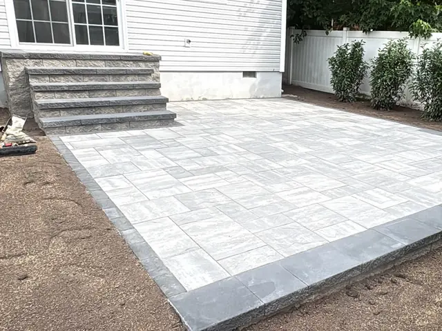 Light gray paver patio with block steps beside a white home