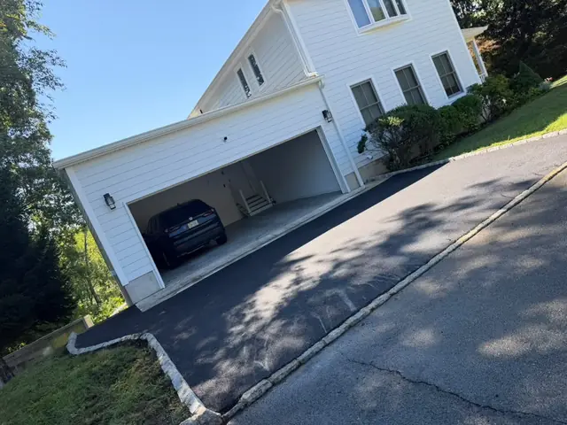 Sloped asphalt driveway with stone curb edging leading to a two-car garage