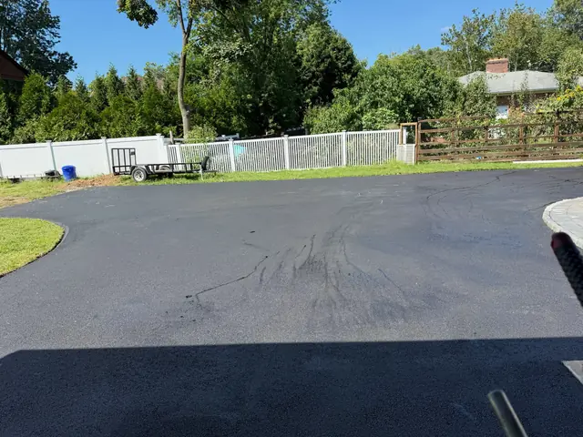 Wide new asphalt driveway with a turnaround area beside a white fence